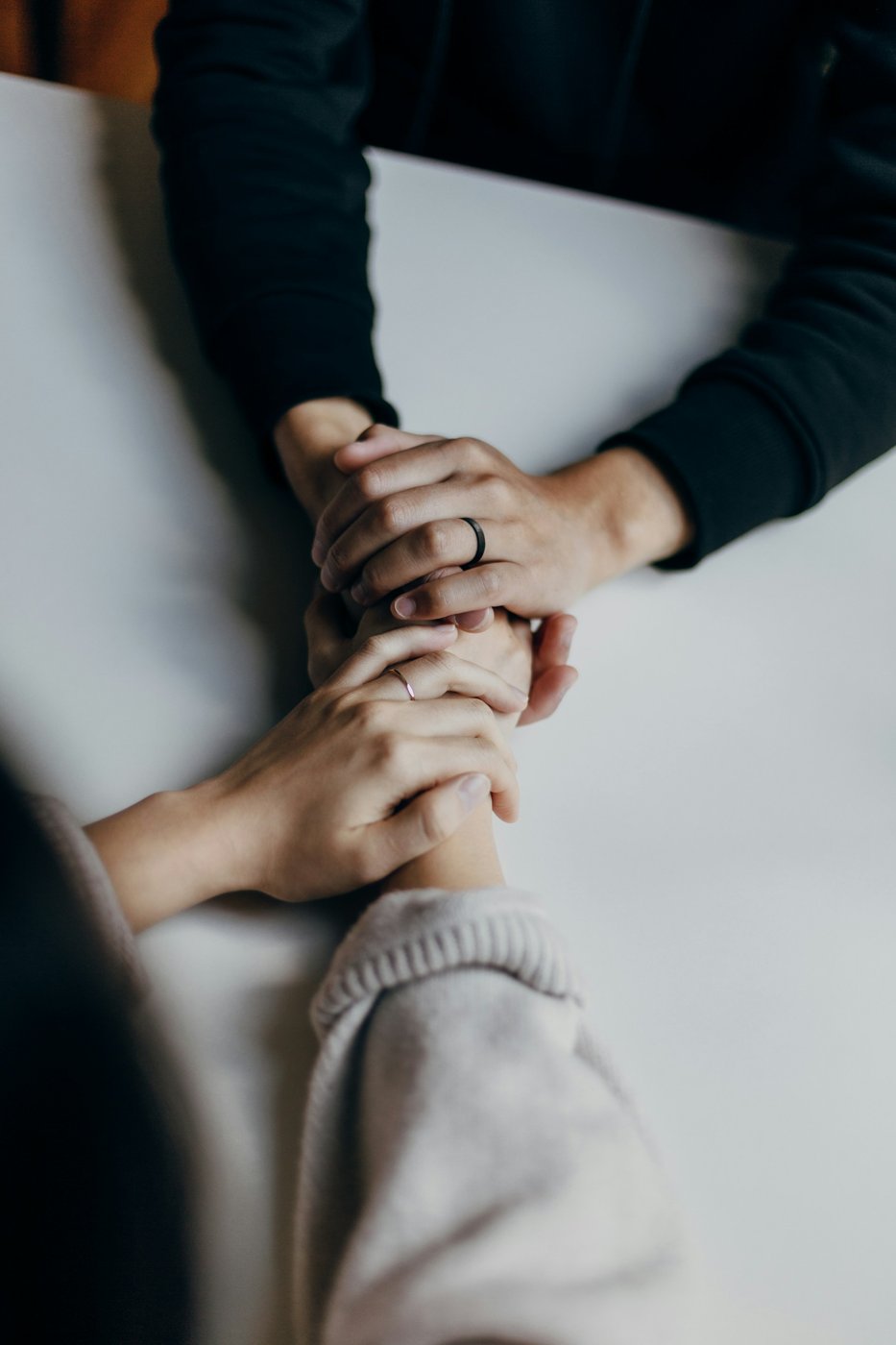 Deux personnes se tenant les mains sur une table, en signe de réconfort